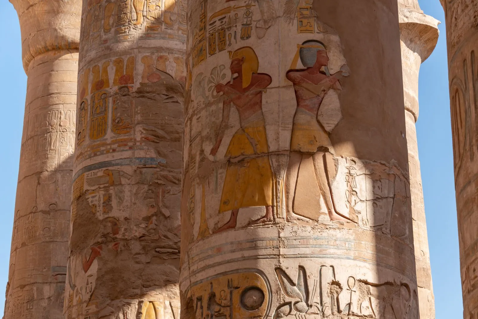 Painted reliefs of figures in yellow and red on the giant columns of Karnak's hypostyle hall