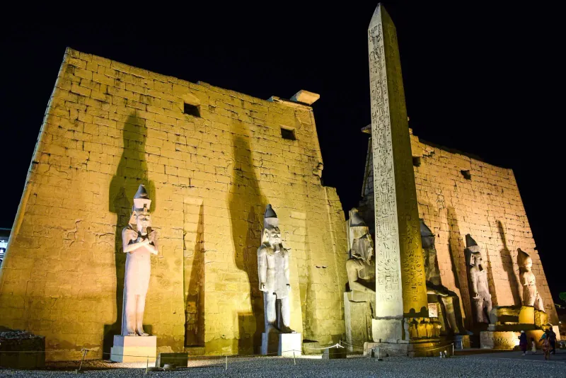 Floodlit first pylon of Luxor Temple at night, with its obelisk and standing statues