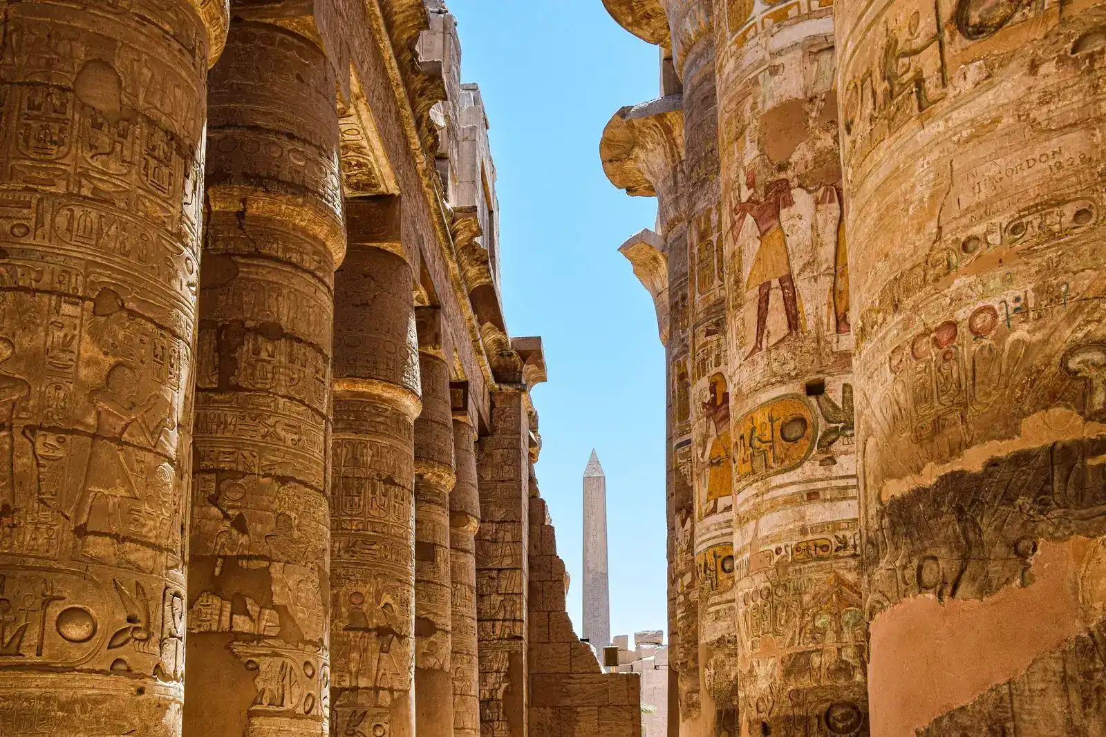 Rows of carved columns in Karnak's hypostyle hall framing an obelisk