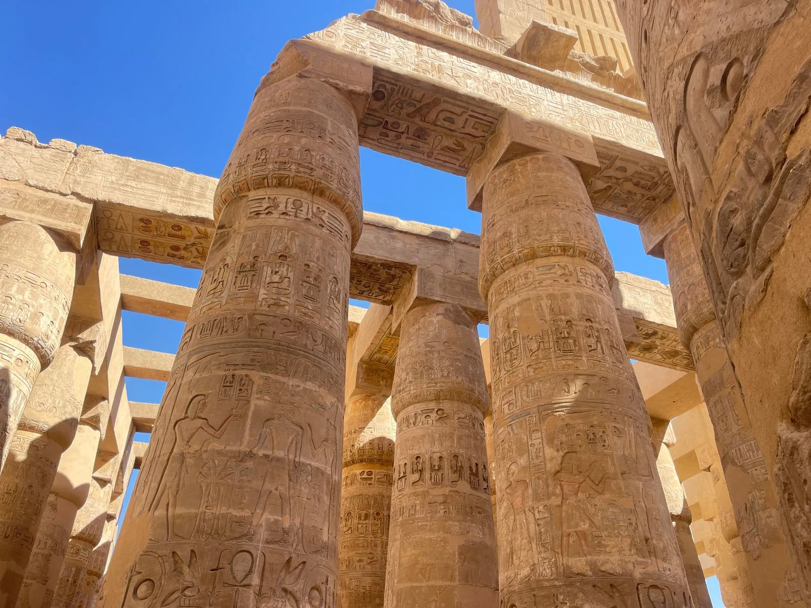 Carved columns and roof beams in Karnak's hypostyle hall under a blue sky