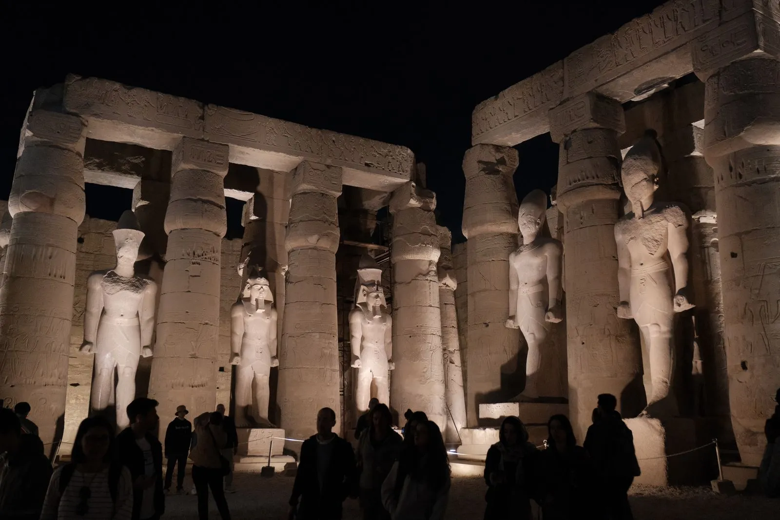 Floodlit statues and columns in the court of Luxor Temple at night, visitors in silhouette