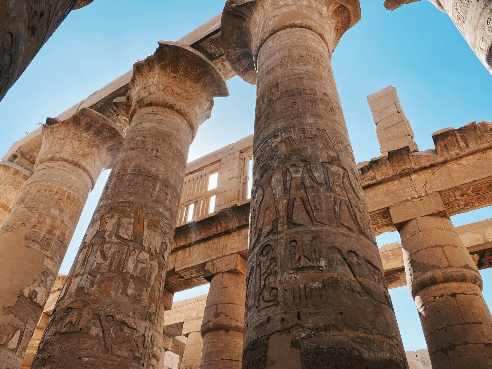 Huge carved columns of Karnak's hypostyle hall with sunlight behind