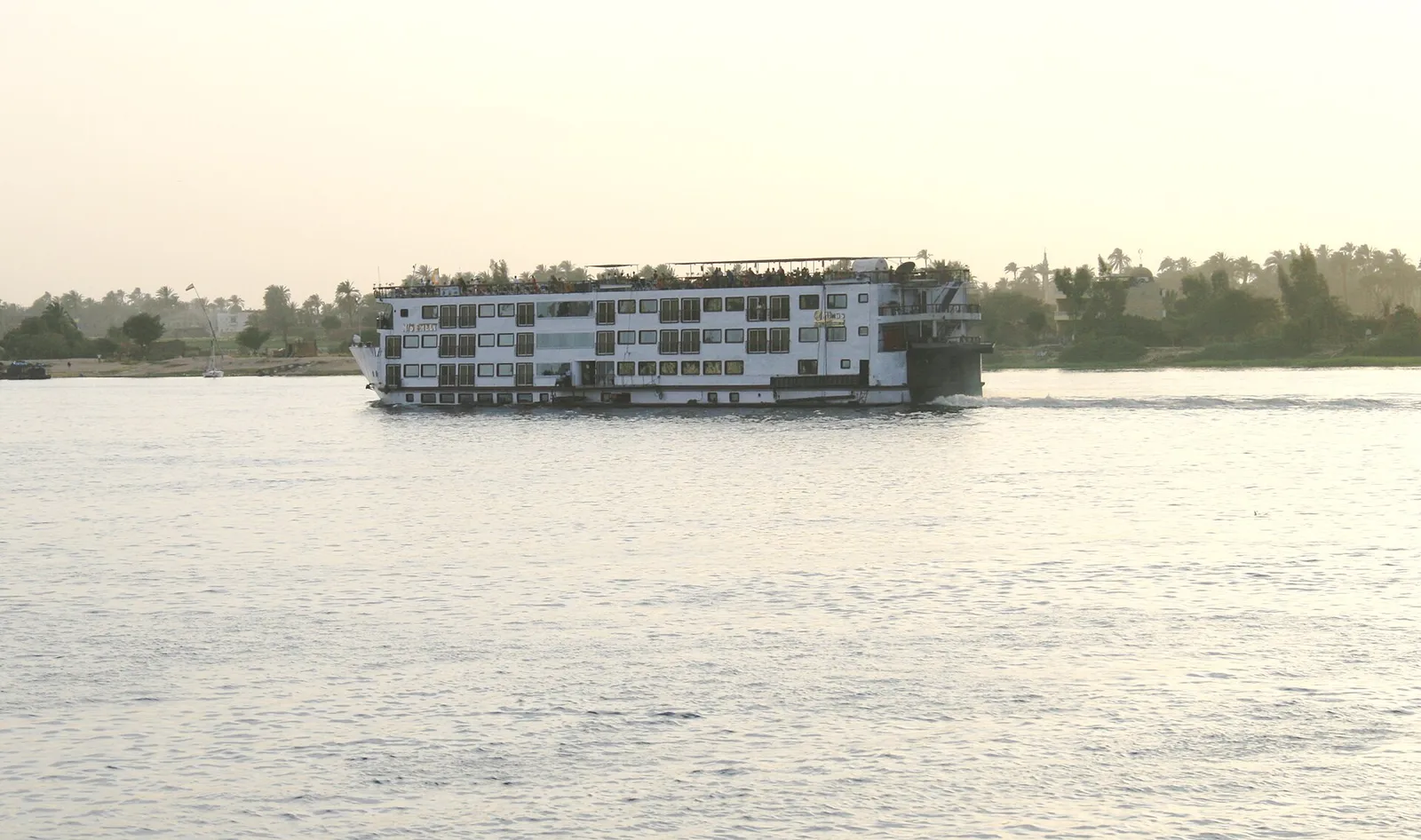 Four-deck cruise ship on the Nile at Luxor in soft evening light, palms behind