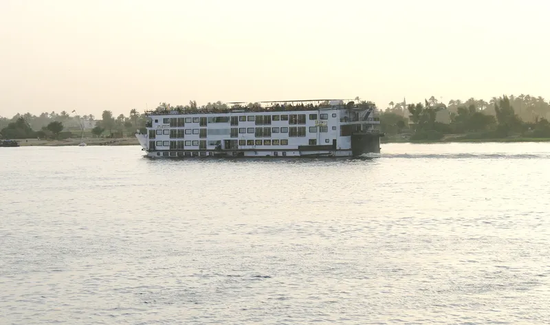 Four-deck cruise ship on the Nile at Luxor in soft evening light, palms behind