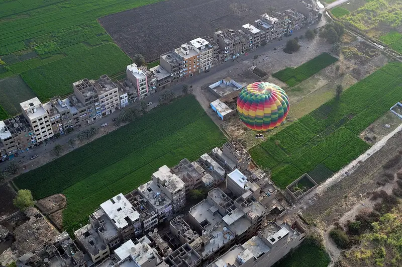 A hot-air balloon landing among green fields and houses on the West Bank, seen from above