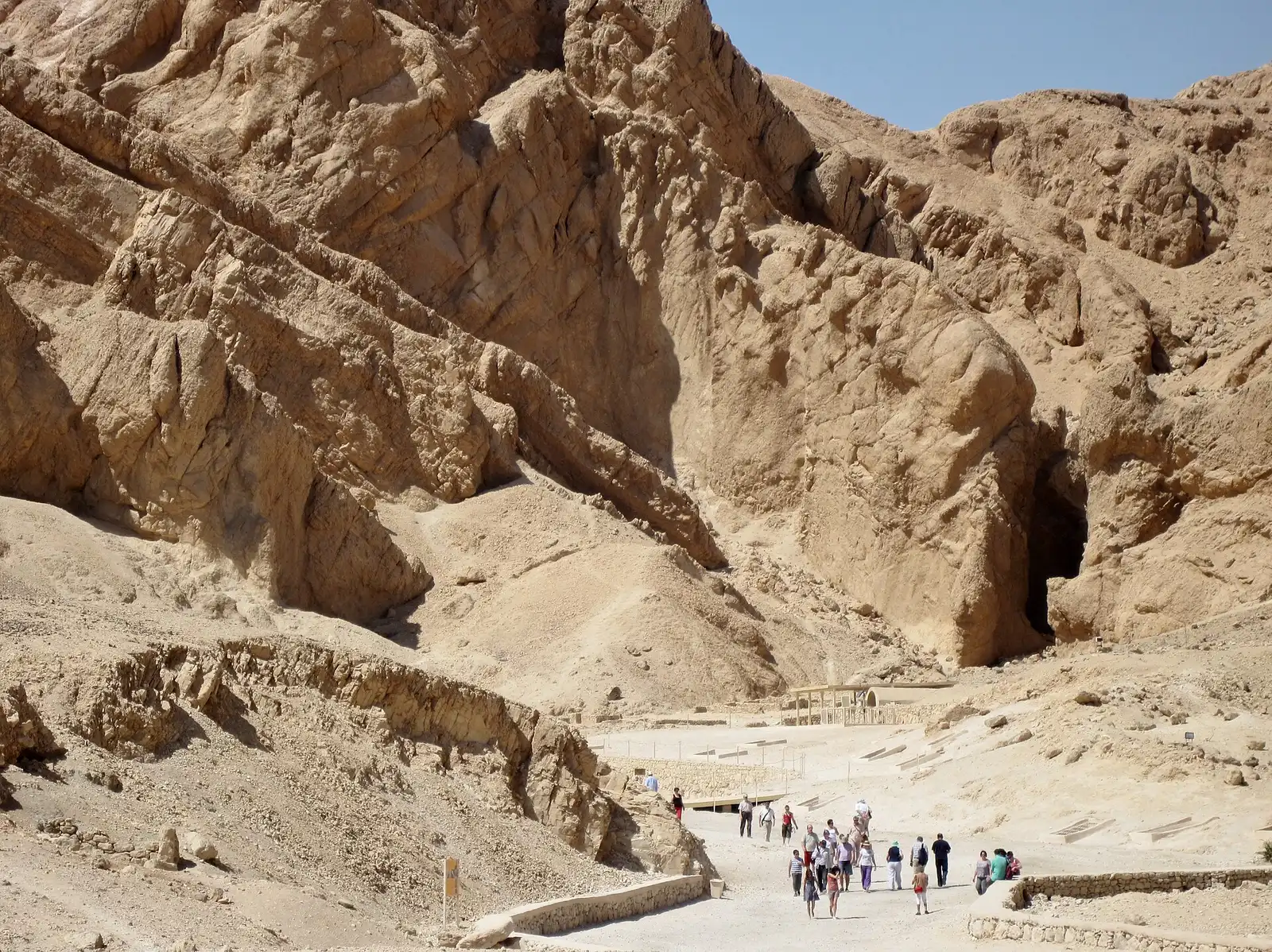 Group of visitors on the paved path at the foot of the Valley of the Queens cliffs