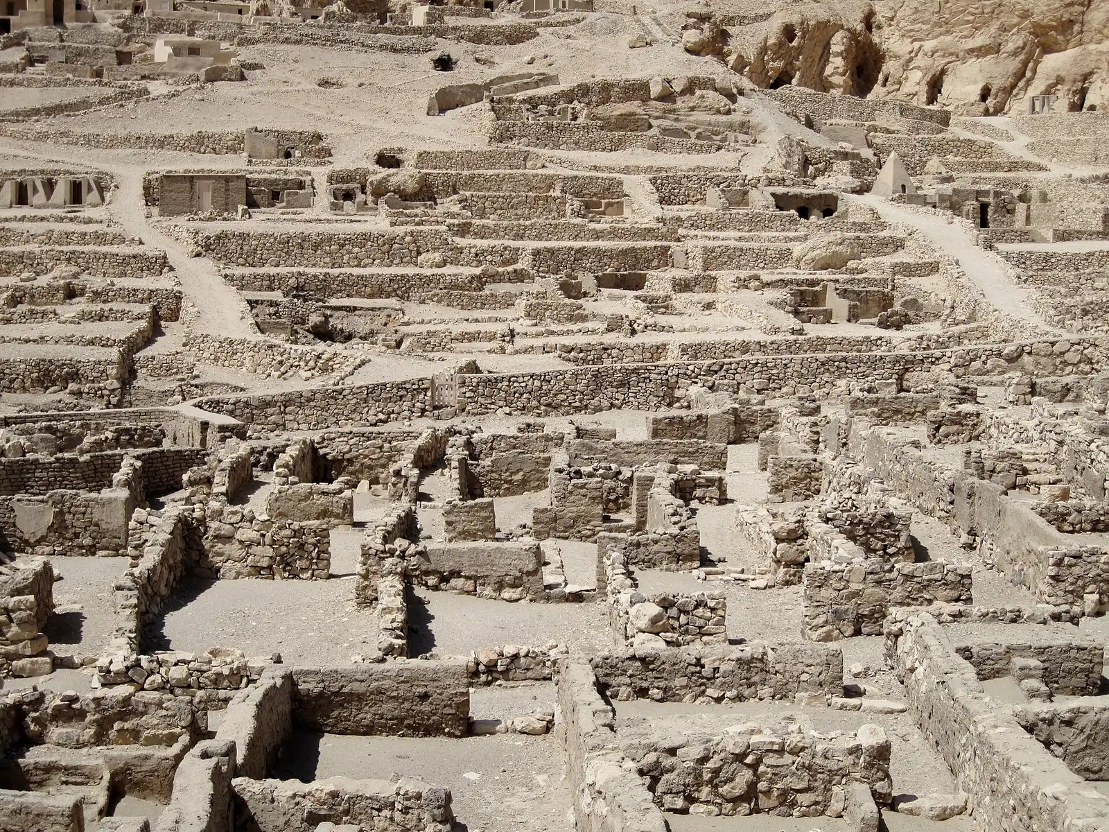 Rows of excavated house walls at Deir el-Medina, with tomb chapels on the slope behind