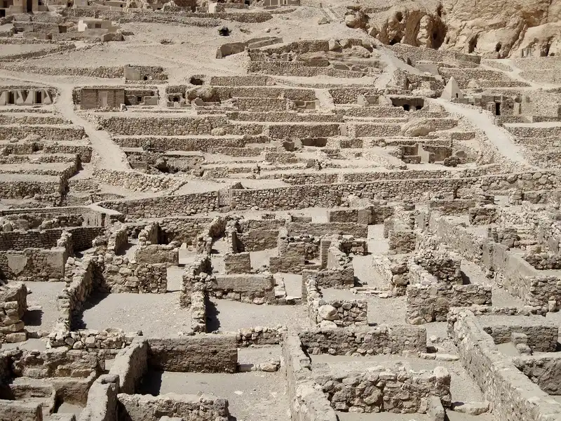 Rows of excavated house walls at Deir el-Medina, with tomb chapels on the slope behind