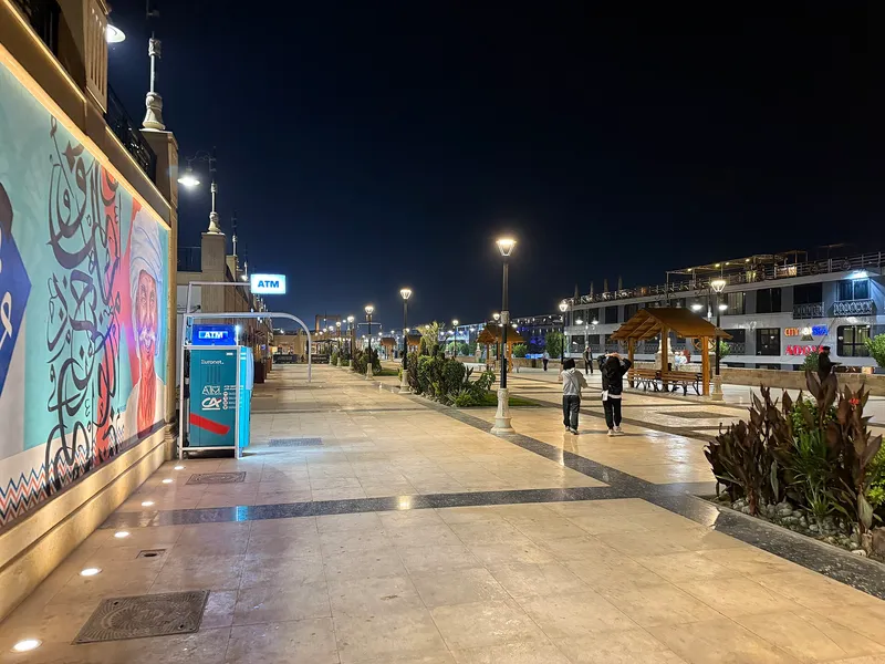 Paved Corniche promenade at night with a painted mural wall and lamps