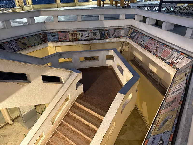 Stairs down to the Mummification Museum's entrance, framed by a mosaic frieze of Egyptian motifs