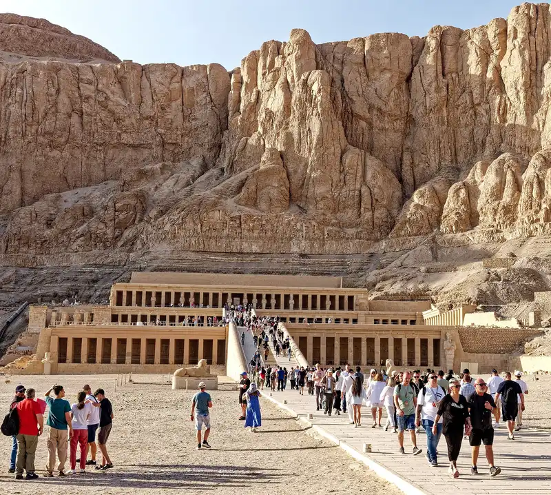 Visitors walking the long causeway toward the terraces of Hatshepsut's temple under the cliffs