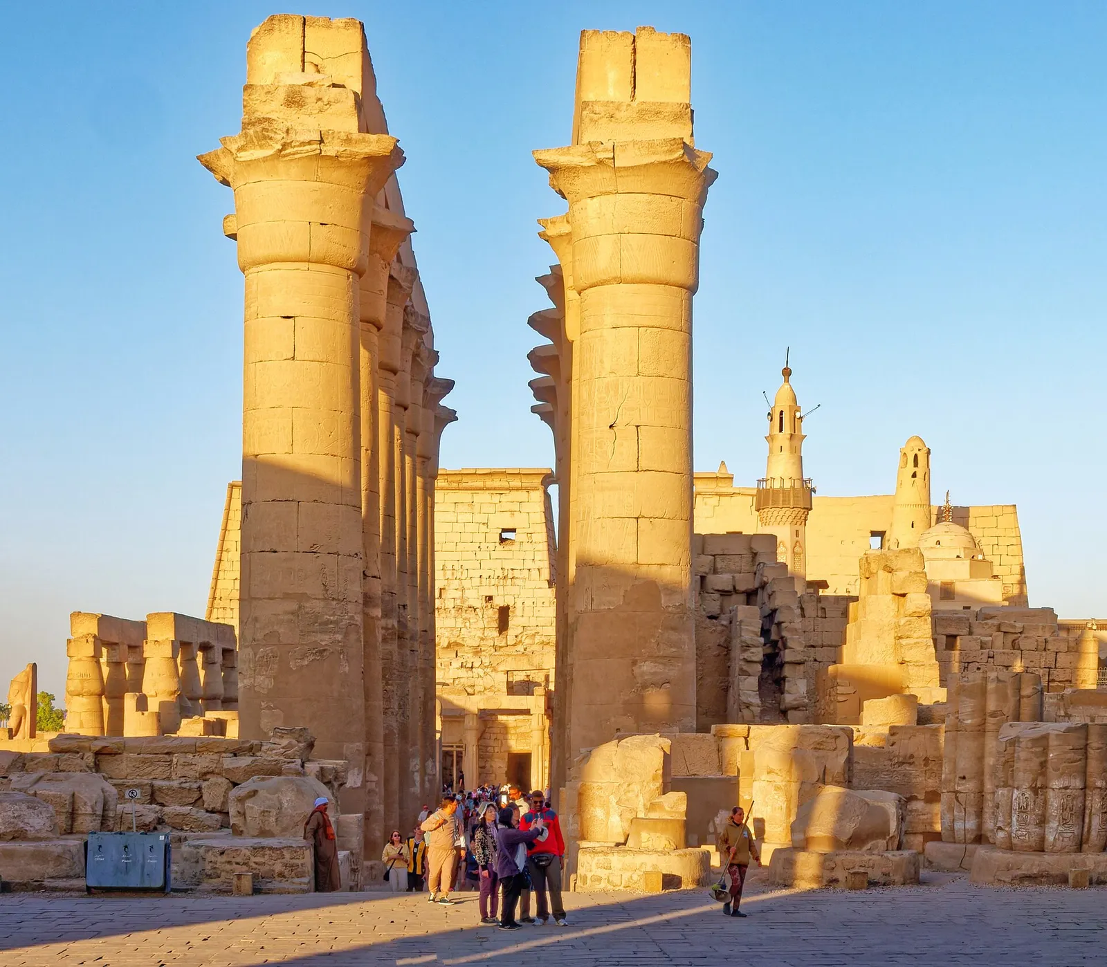 Tall columns of Luxor Temple in warm light with the Abu Haggag mosque behind