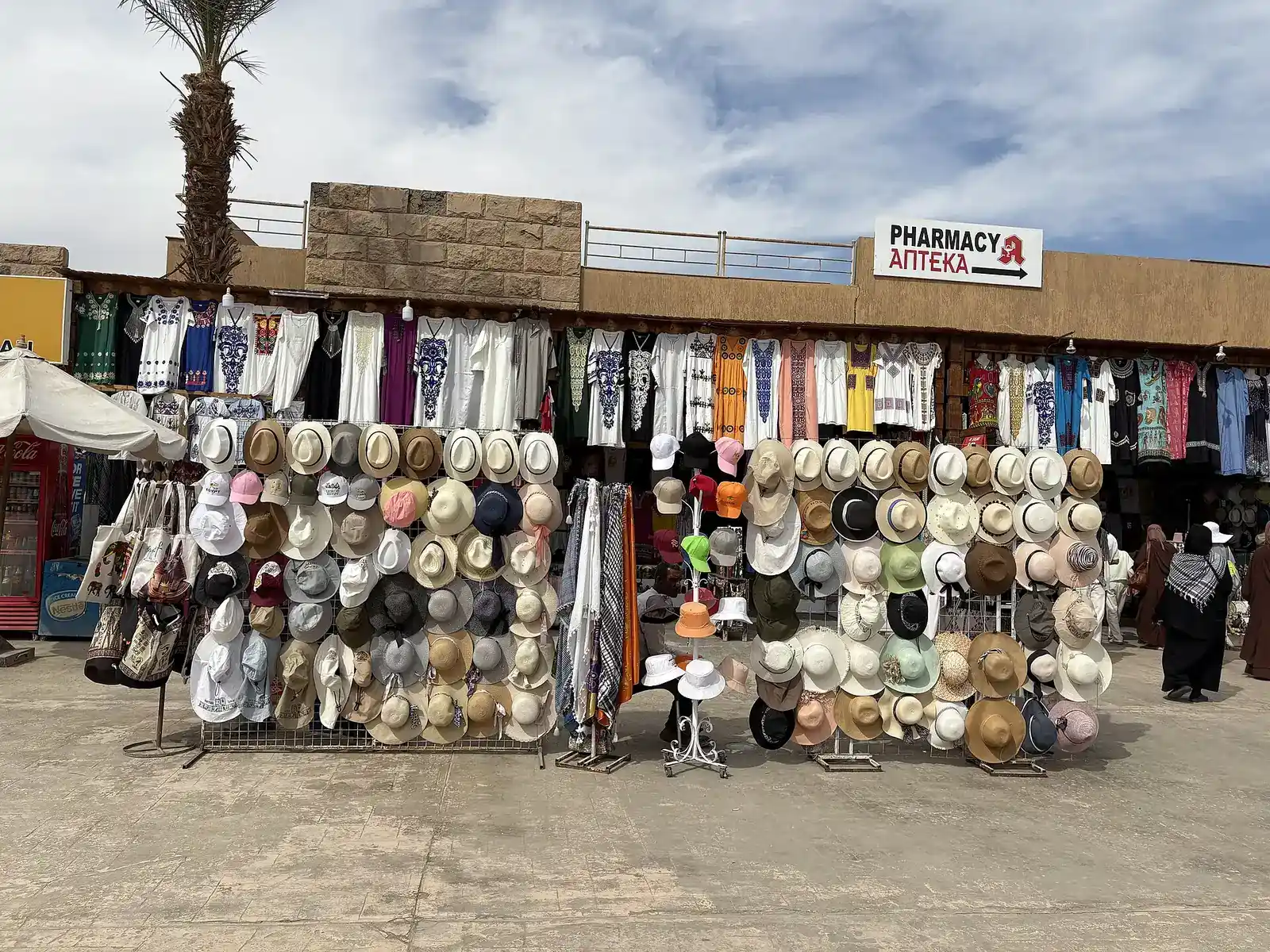 Row of souvenir stalls with tunics and sun hats under a cloudy sky
