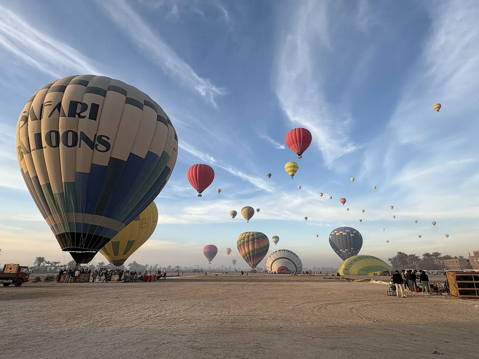 Balloons rising from a wide sandy field at sunrise