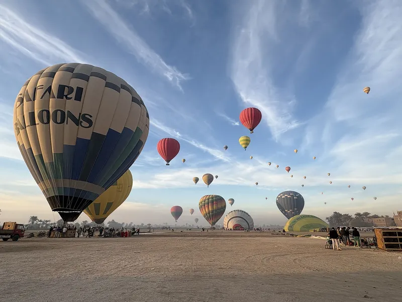 Balloons rising from a wide sandy field at sunrise