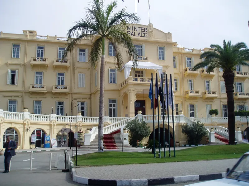 Yellow facade of the Winter Palace hotel with its double staircase and palms
