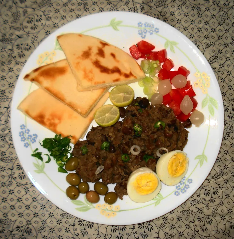 Plate of ful medames with boiled egg, olives, tomato, lime and flatbread