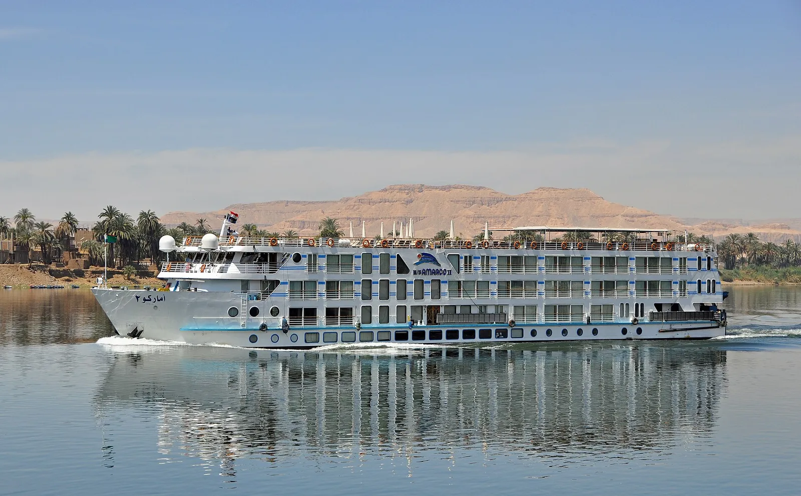White cruise ship on the Nile, its reflection in calm water, the West Bank hills behind