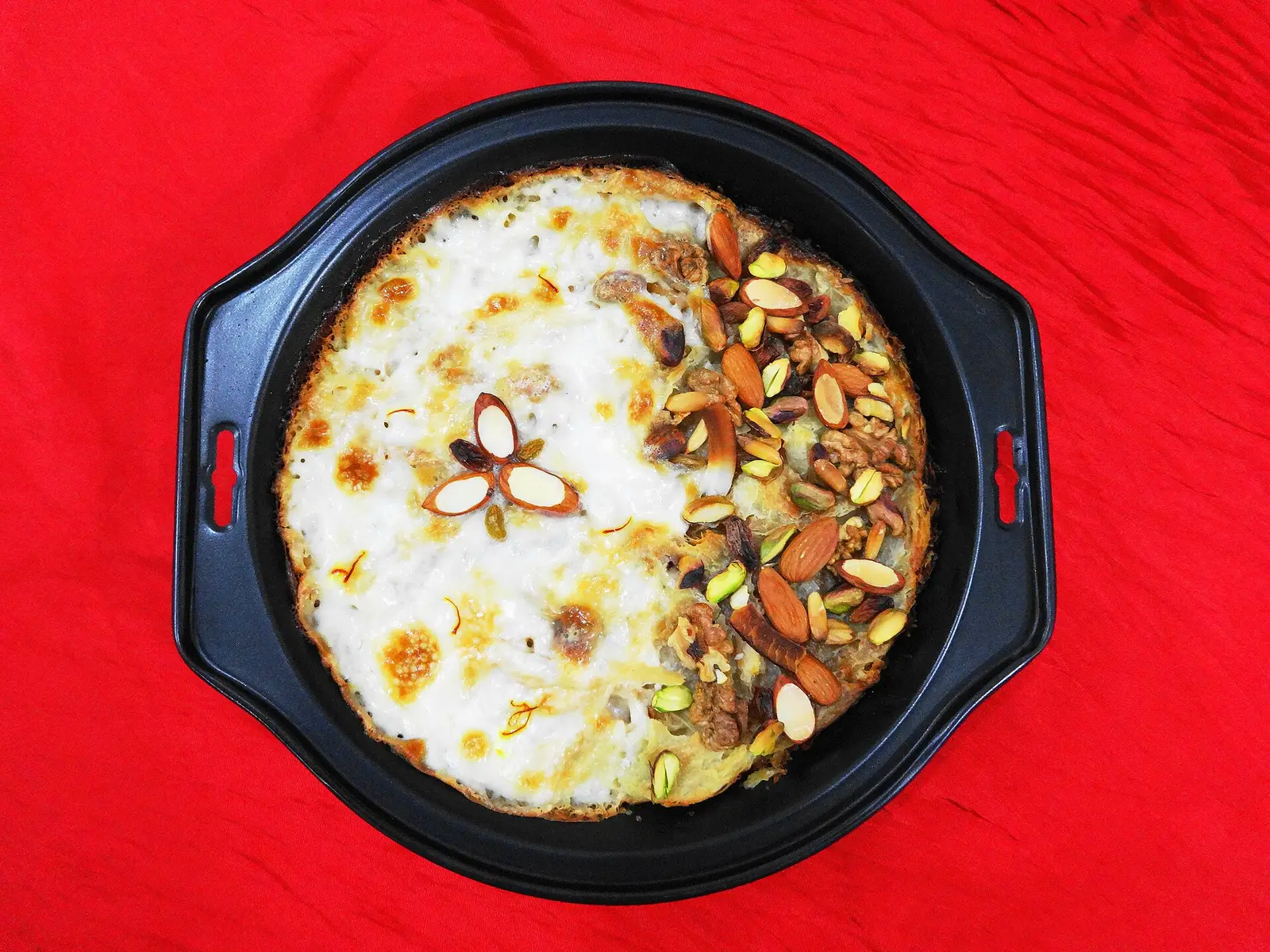 Baked umm ali in a round dish, half topped with almonds and pistachios