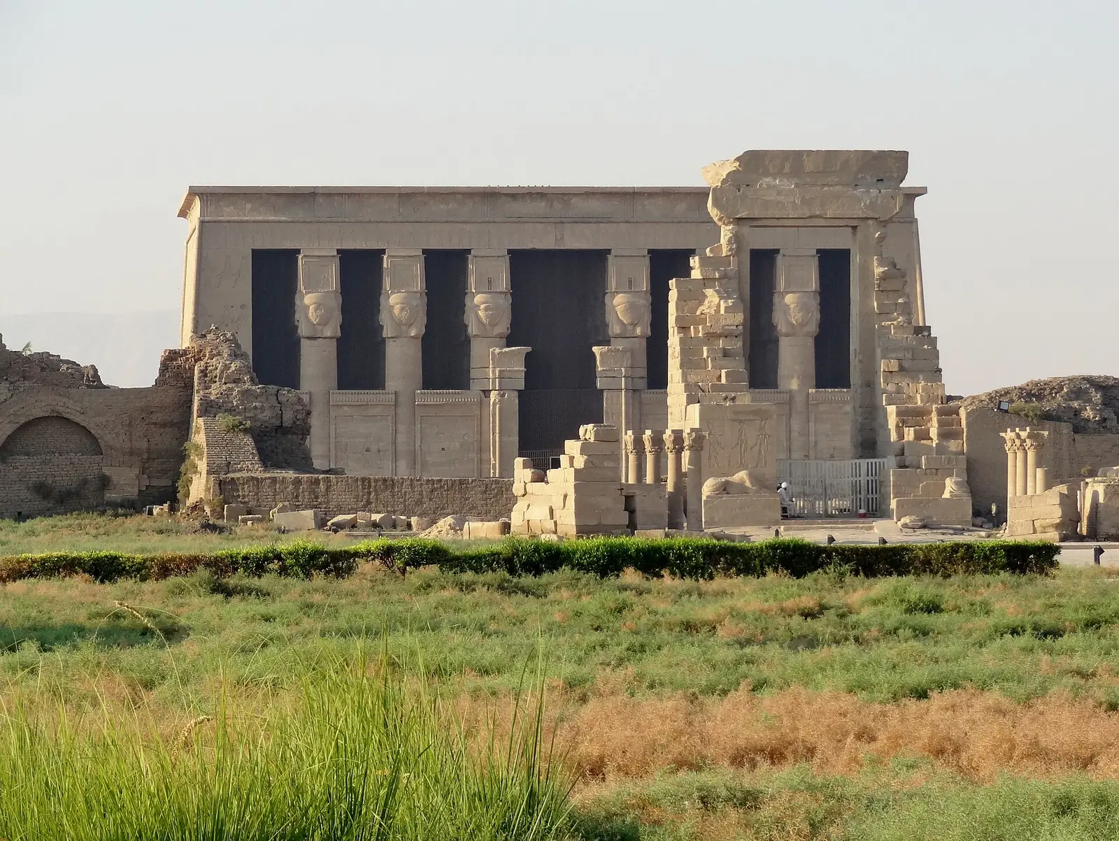 Hathor-headed columns on the front of the Dendera temple, with ruined gateways in front
