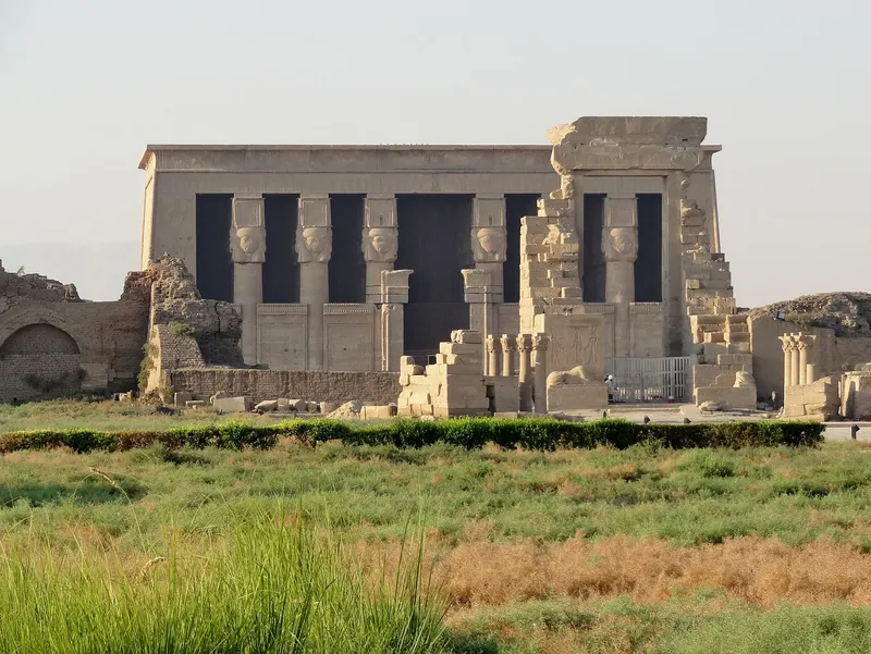 Hathor-headed columns on the front of the Dendera temple, with ruined gateways in front