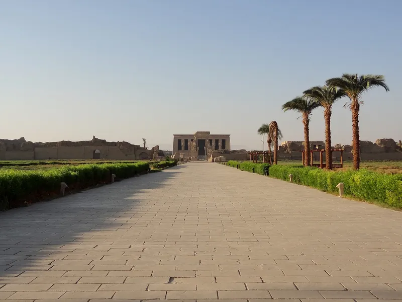 Long paved walkway lined with palms leading to the Dendera temple facade