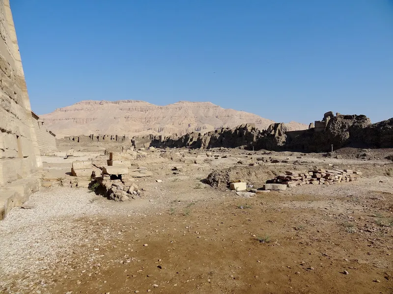 Inside the Medinet Habu precinct: temple wall, scattered blocks and mud-brick ruins below the hills