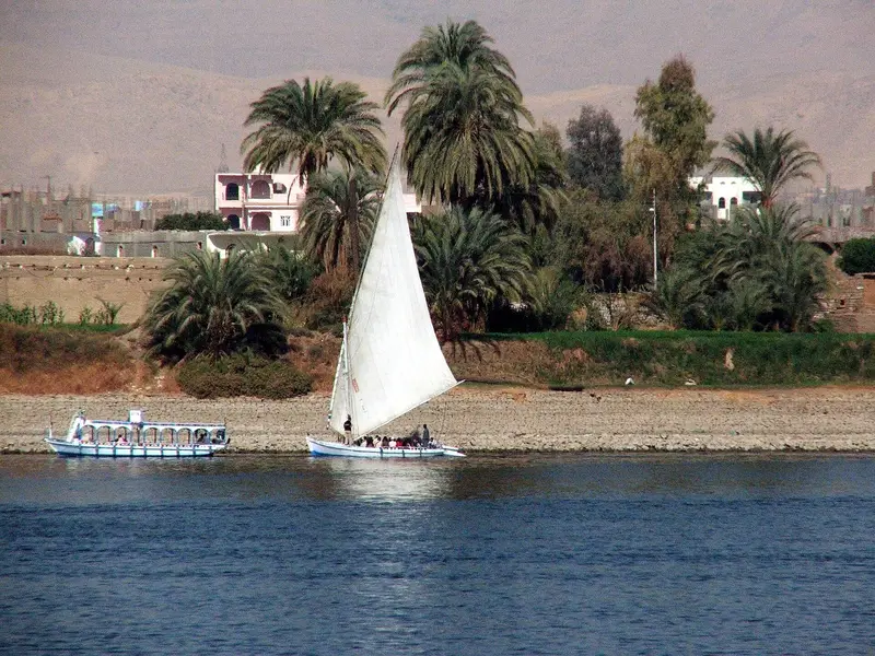 Felucca and a small river boat along the Luxor West Bank shore, palms behind