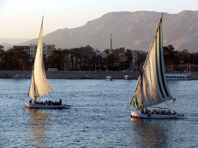 Two feluccas full of passengers on the Nile at Luxor in late-afternoon light, a minaret and hills behind
