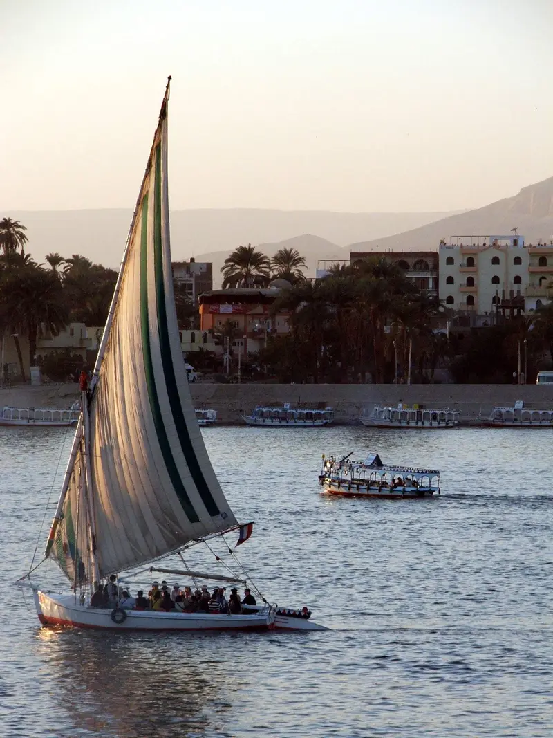 Felucca with a striped sail on the Nile at Luxor, the riverfront hotels behind