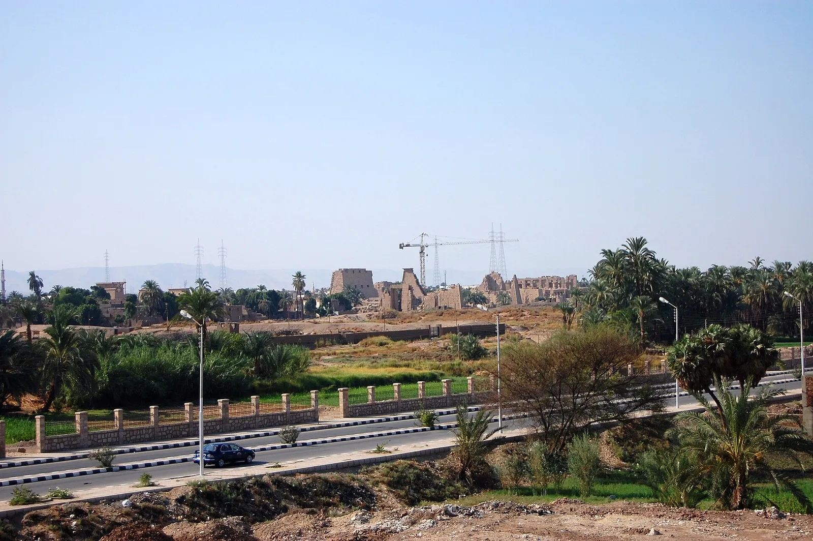 Distant view of Karnak's ruins beyond a road and palms