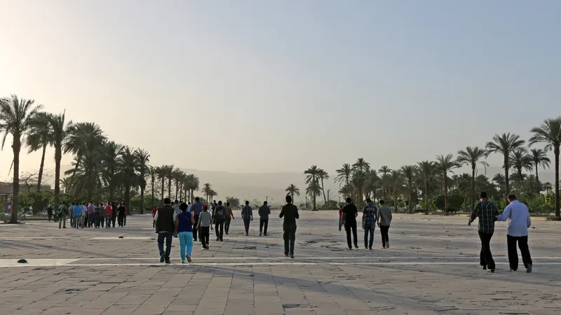 Visitors walking across the wide palm-lined entrance plaza toward Karnak in hazy morning light