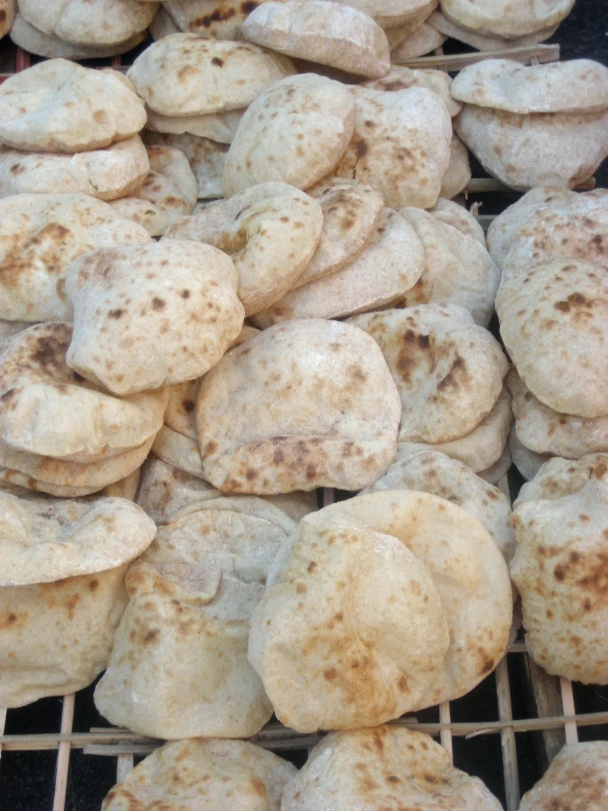 Stacks of puffed round baladi flatbread on a wooden rack