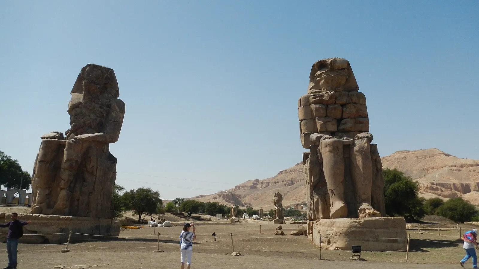 The Colossi of Memnon seen from the roadside, with a few visitors at their feet