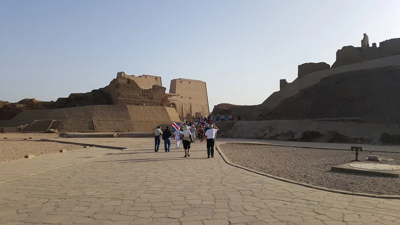 Visitors seen from behind on the paved approach to the pylon of Edfu temple