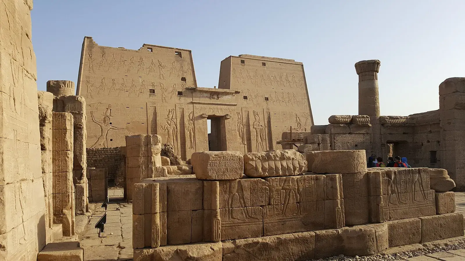 The carved pylon of Edfu temple behind fallen relief blocks in the late afternoon sun