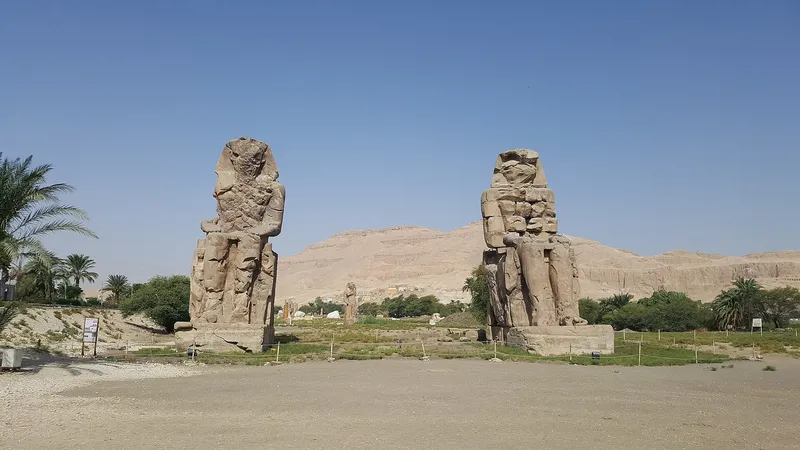 The two Colossi of Memnon framed by palms, with the West Bank cliffs beyond