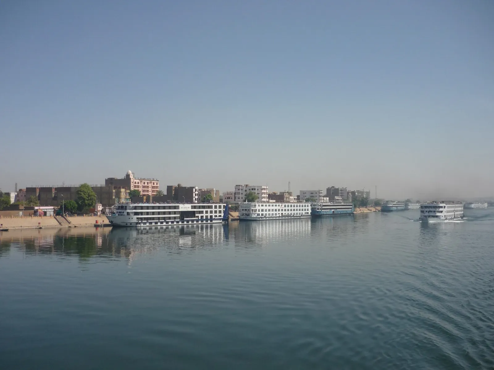 Cruise ships moored along the Edfu riverfront, another one under way on the Nile