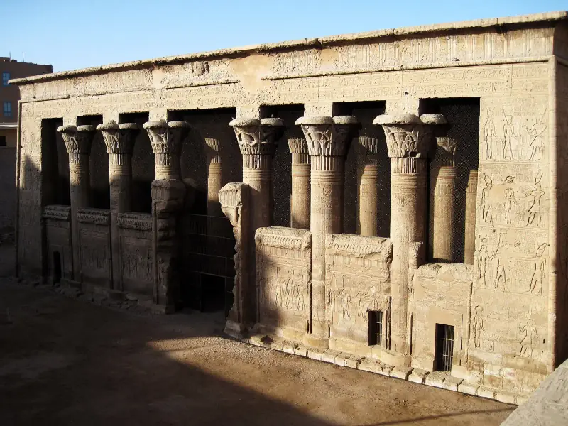 The columned front of Esna temple's hall in its pit below the modern town, lit by low sun
