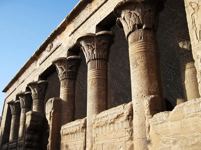 A row of carved columns along the front of Esna temple against a blue sky