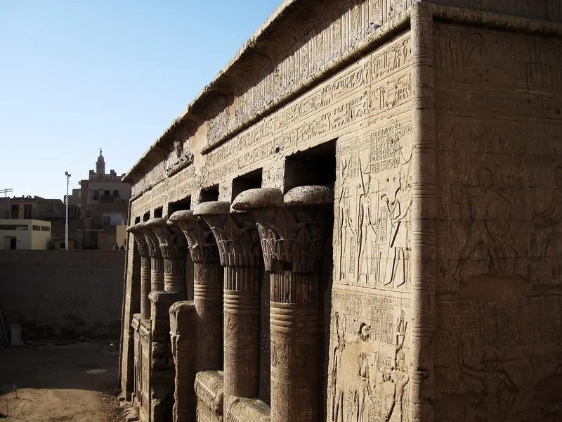 Esna temple's carved columns with a minaret and town houses behind